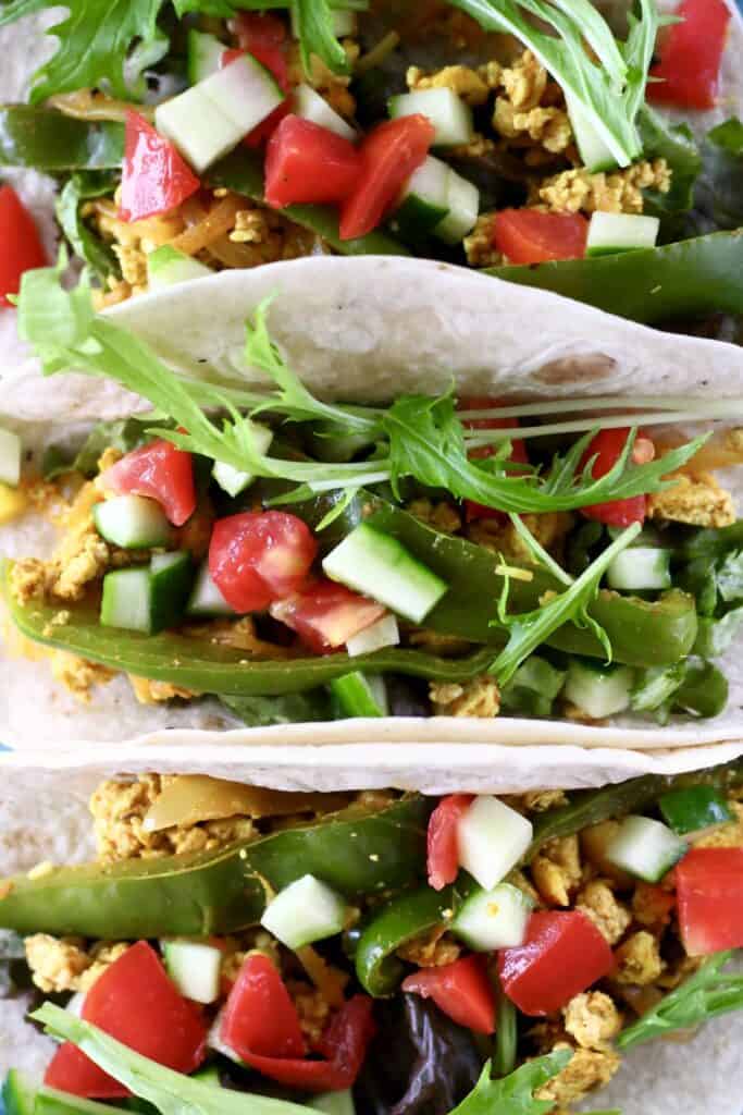 Close-up photo from above of three tacos filled with scrambled tofu, lettuce, cucumber and tomatoes