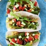 Close-up photo from above of three tacos filled with scrambled tofu, lettuce, cucumber and tomatoes