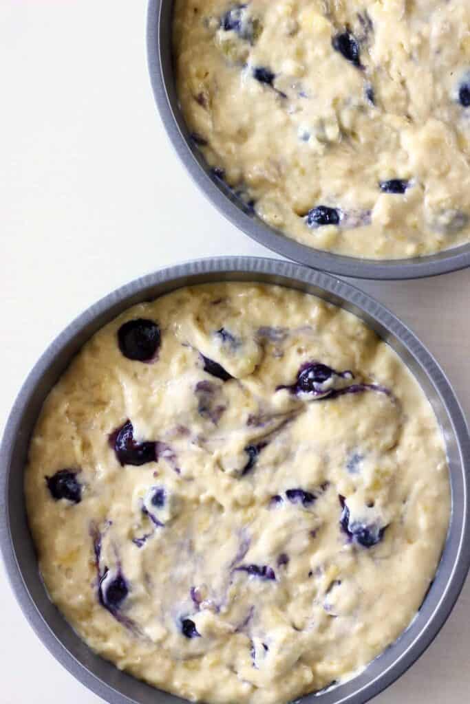 Photo of two cake tins taken from above filled with cake batter dotted with blueberries