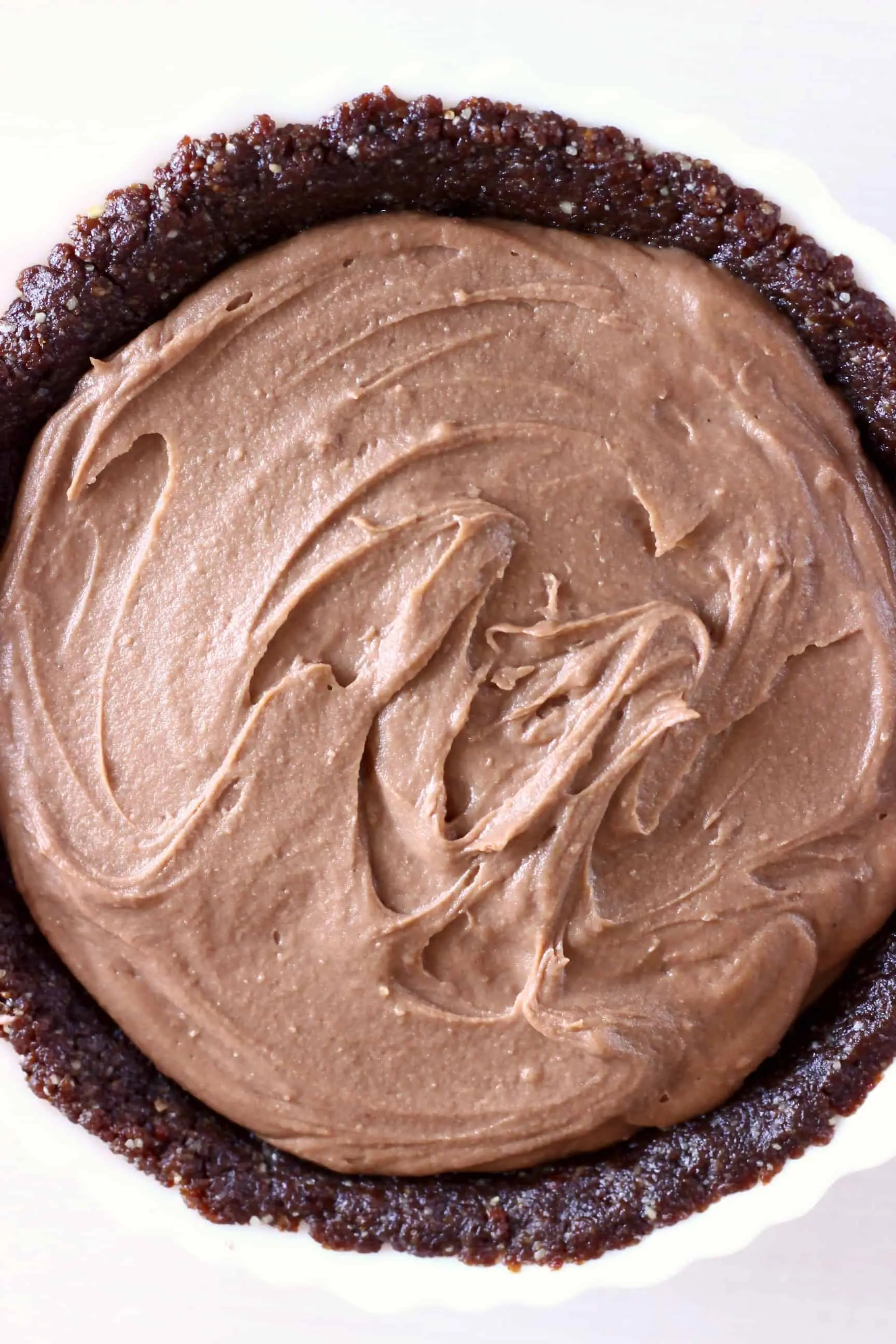 Chocolate pie crust filled with chocolate filling in a white pie dish against a white background