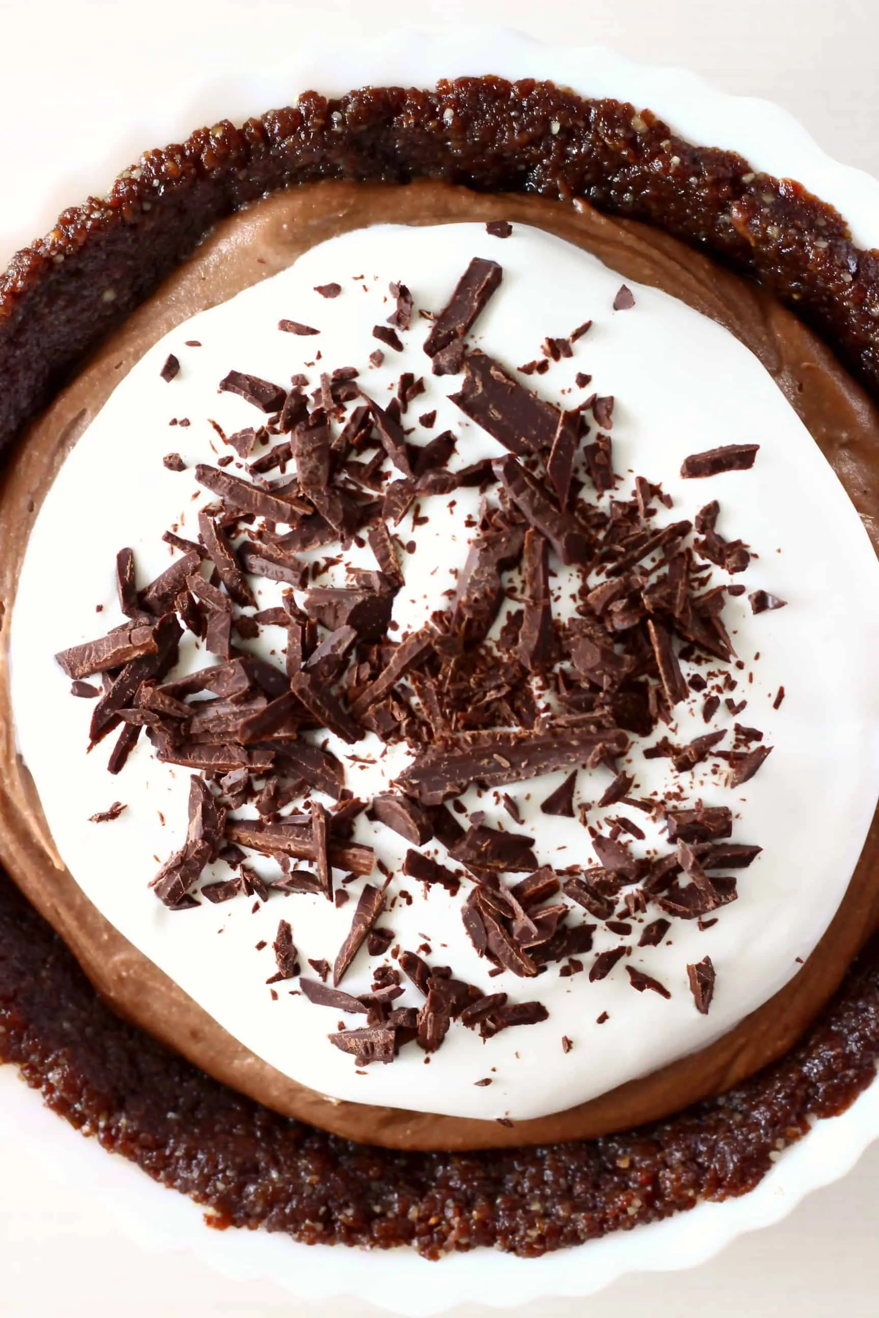 Chocolate pie topped with whipped cream and chocolate shavings in a white pie dish against a white background