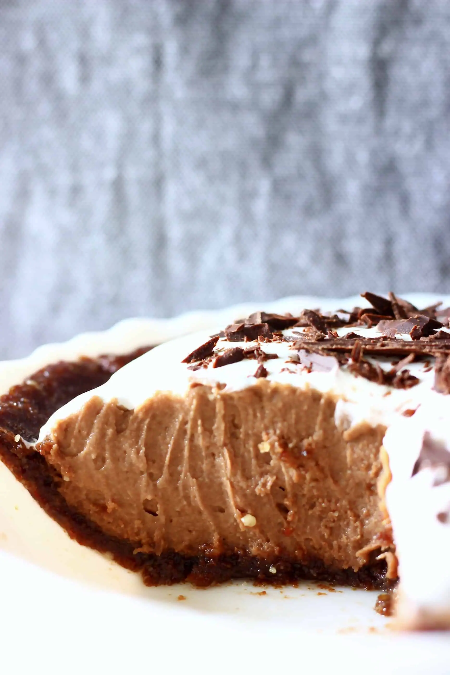 Chocolate pie in a pie dish against a grey fabric background with a slice cut out of it