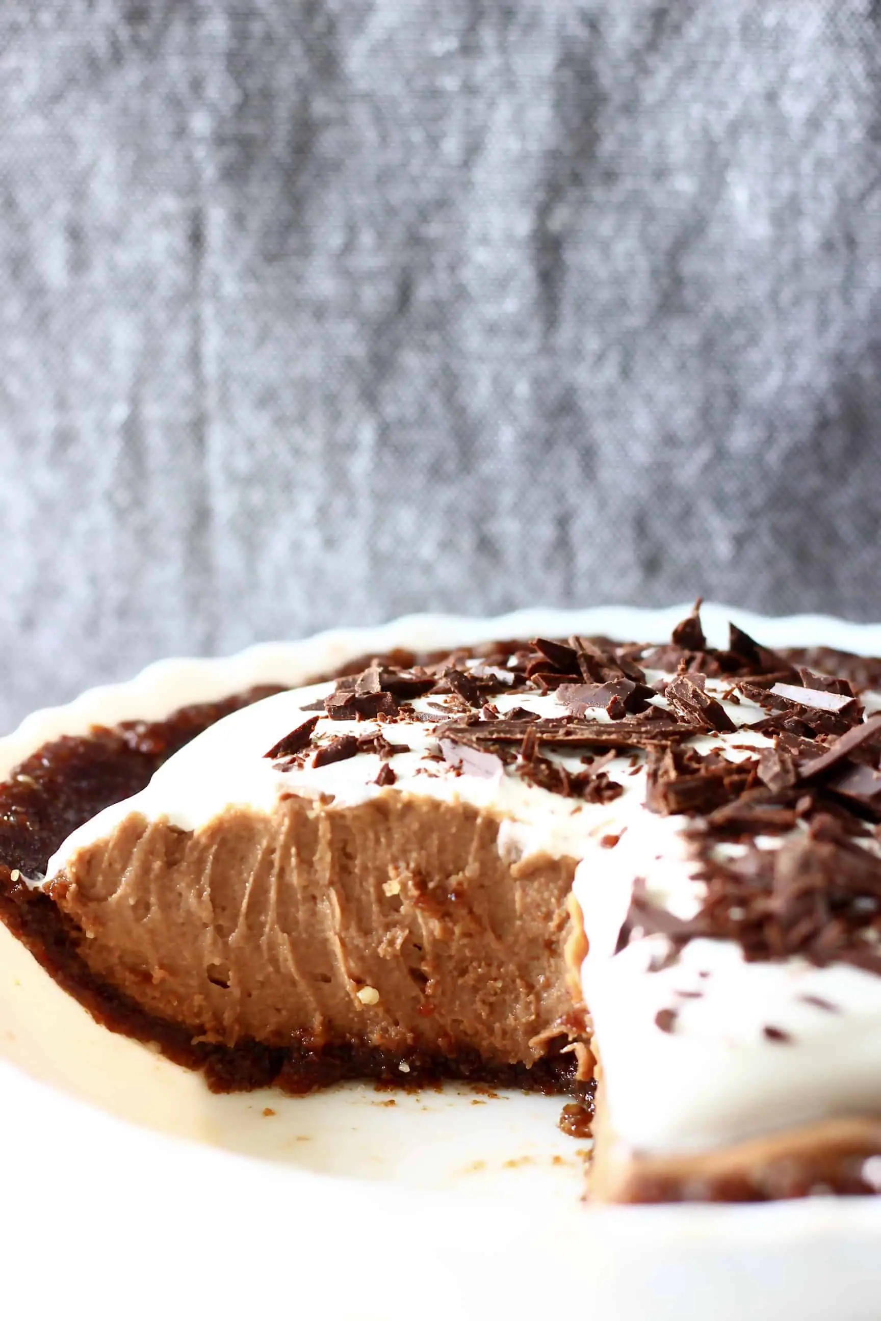 Chocolate pie in a pie dish against a grey fabric background with a slice cut out of it