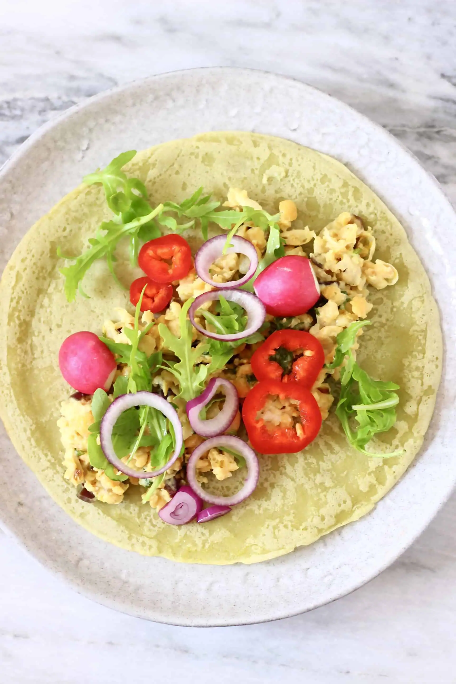 A green wrap on a plate, topped with chickpeas and salad