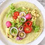 A green wrap on a plate, topped with chickpeas and salad
