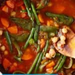 Photo of a chickpea and vegetable tomato stew in a saucepan with a wooden spatula holding up some chickpeas