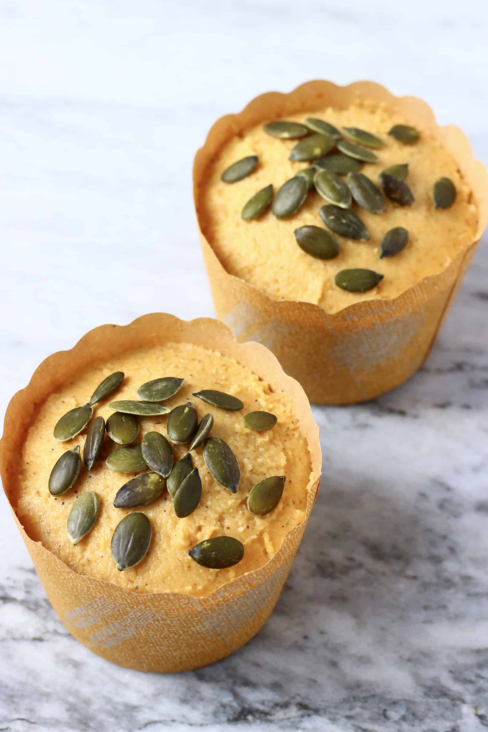Raw gluten-free vegan pumpkin muffin batter in two muffin cases topped with pumpkin seeds