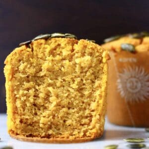Two gluten-free vegan pumpkin muffins topped with pumpkin seeds, with one cut in half
