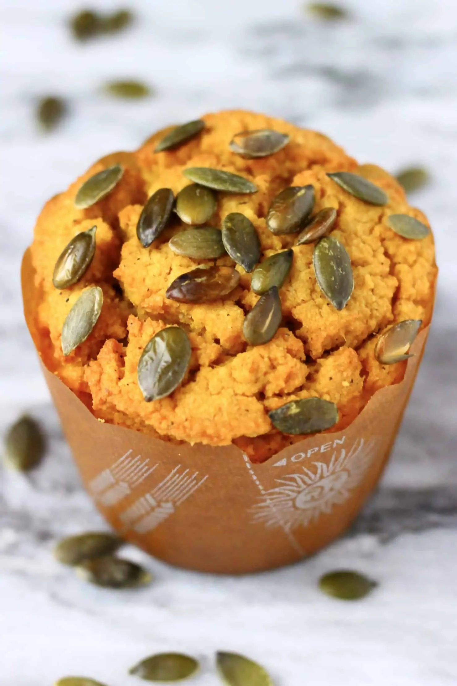 A gluten-free vegan pumpkin muffin in a muffin case topped with pumpkin seeds