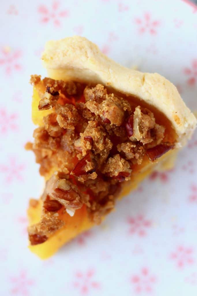 Photo of a slice of peach pie with streusel topping on a white plate