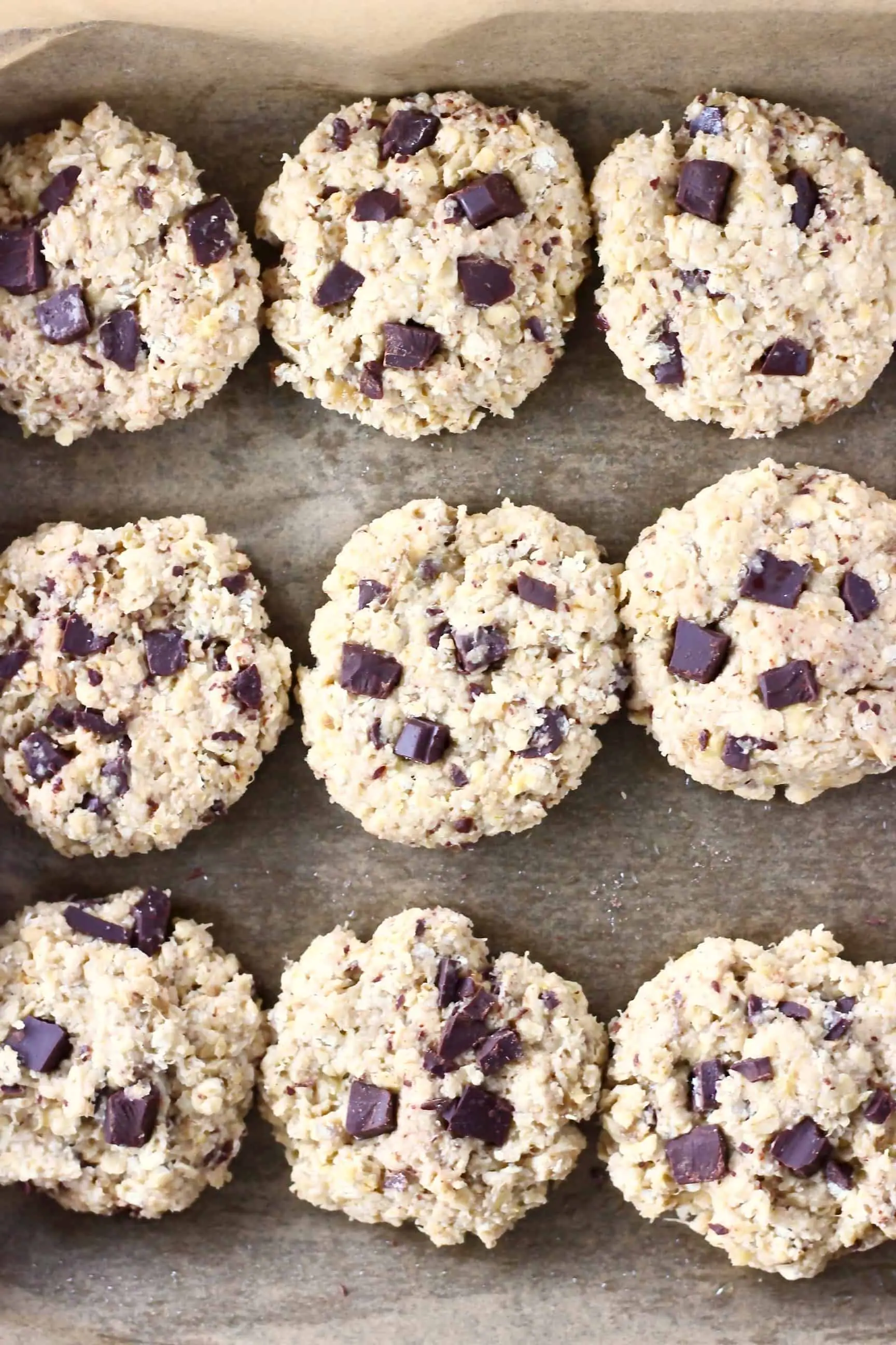 Nine raw gluten-free vegan banana oatmeal cookies with chocolate chips on a baking tray lined with baking paper