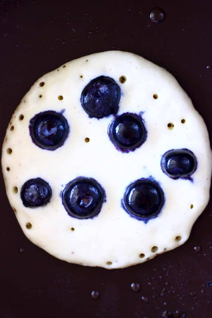 Photo of a pancake with blueberries in it being cooked in a frying pan
