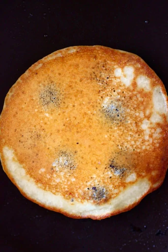 Photo of a golden brown pancake being cooked in a frying pan