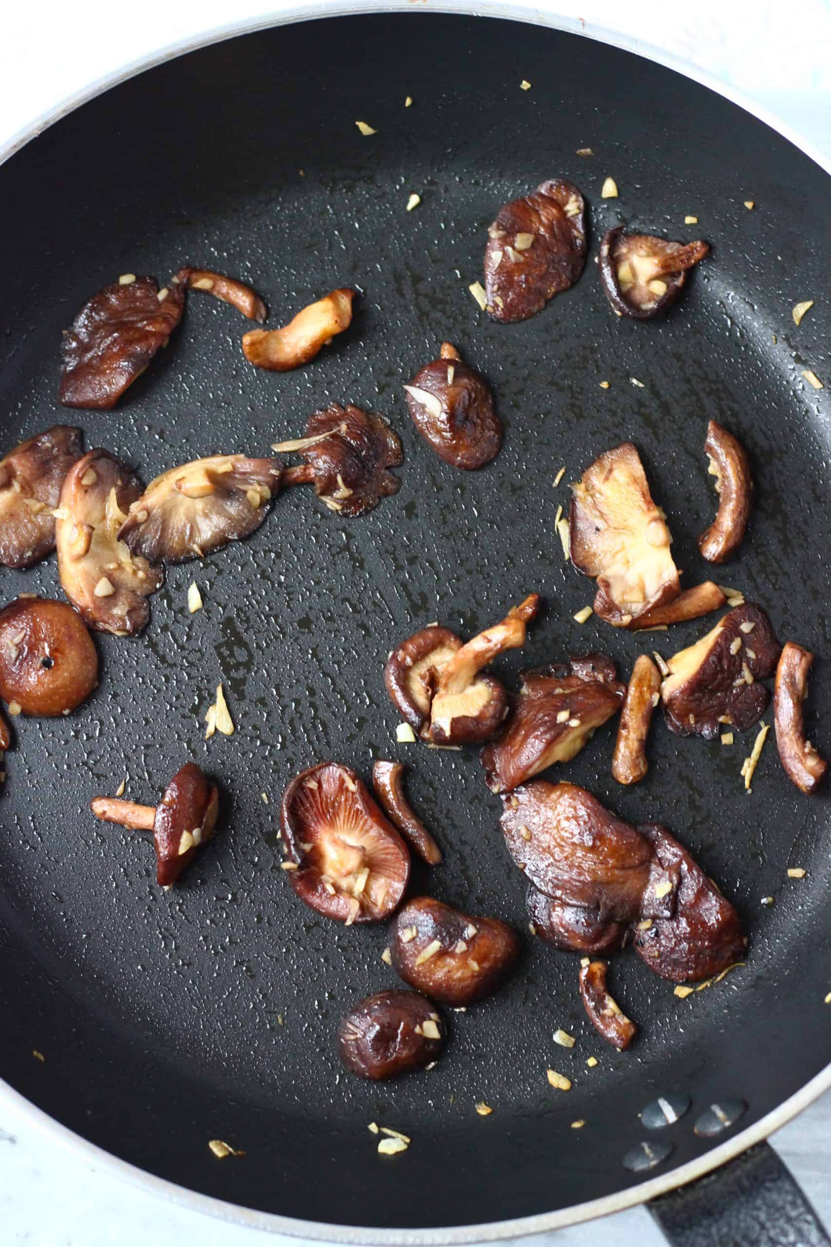 Minced garlic and shiitake mushrooms being cooked in a black frying pan