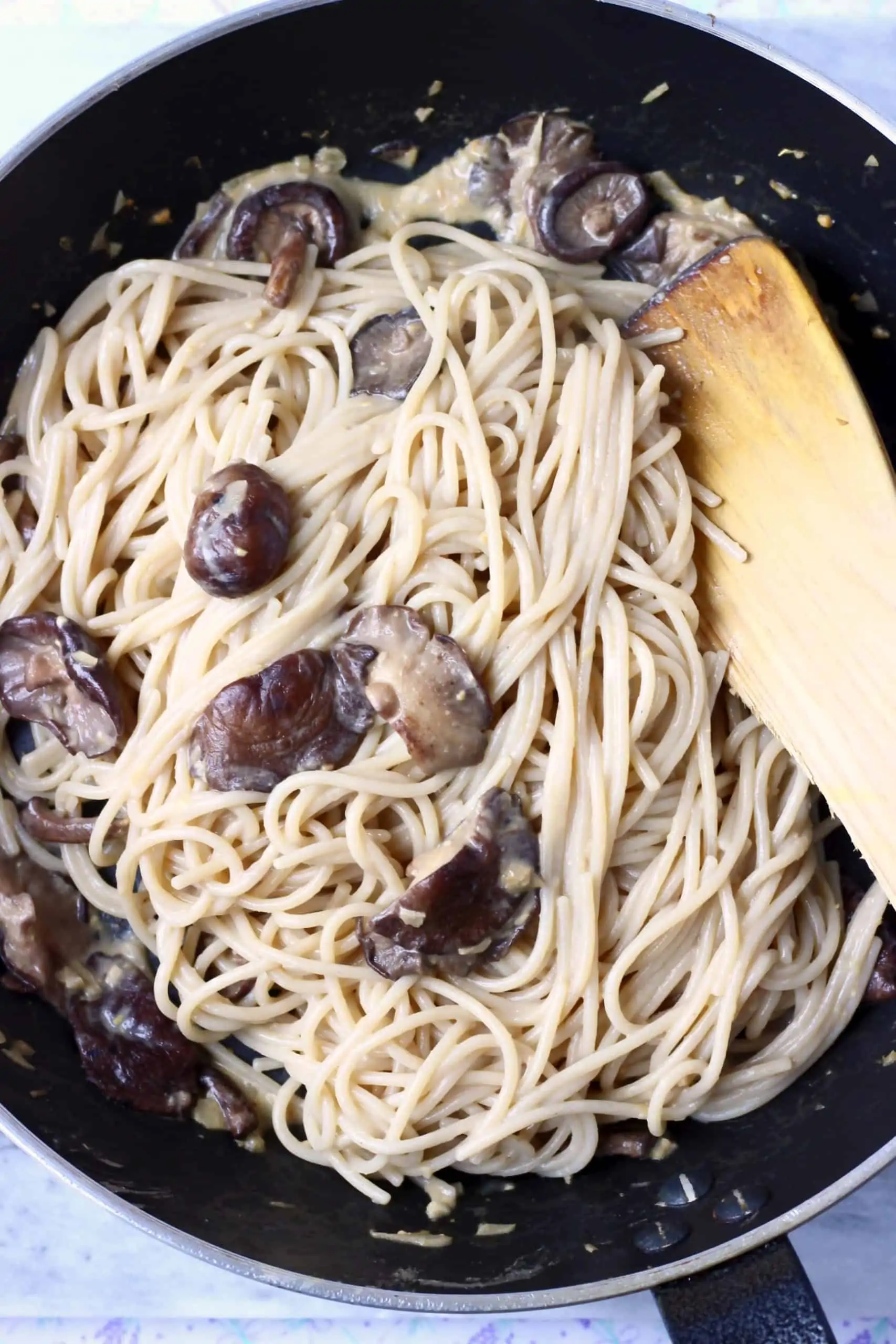 Creamy vegan miso pasta sauce with spaghetti and shiitake mushrooms being mixed together in a black frying pan