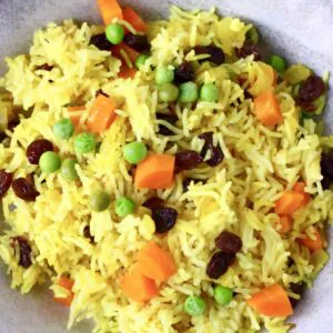 Photo of yellow rice with vegetables in a ceramic bowl against a grey background