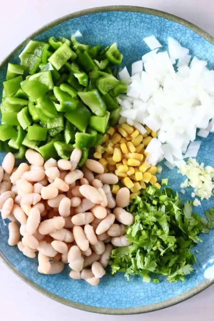 Photo of a blue plate topped with chopped green pepper, white beans, sweetcorn, chopped coriander, diced onion and minced garlic
