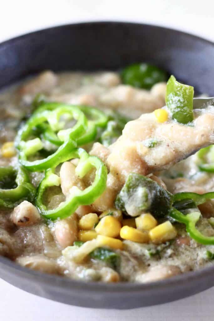 Photo of a dark grey bowl containing white stew with white beans, sweetcorn and green pepper with a spoon lifting up a mouthful of the stew