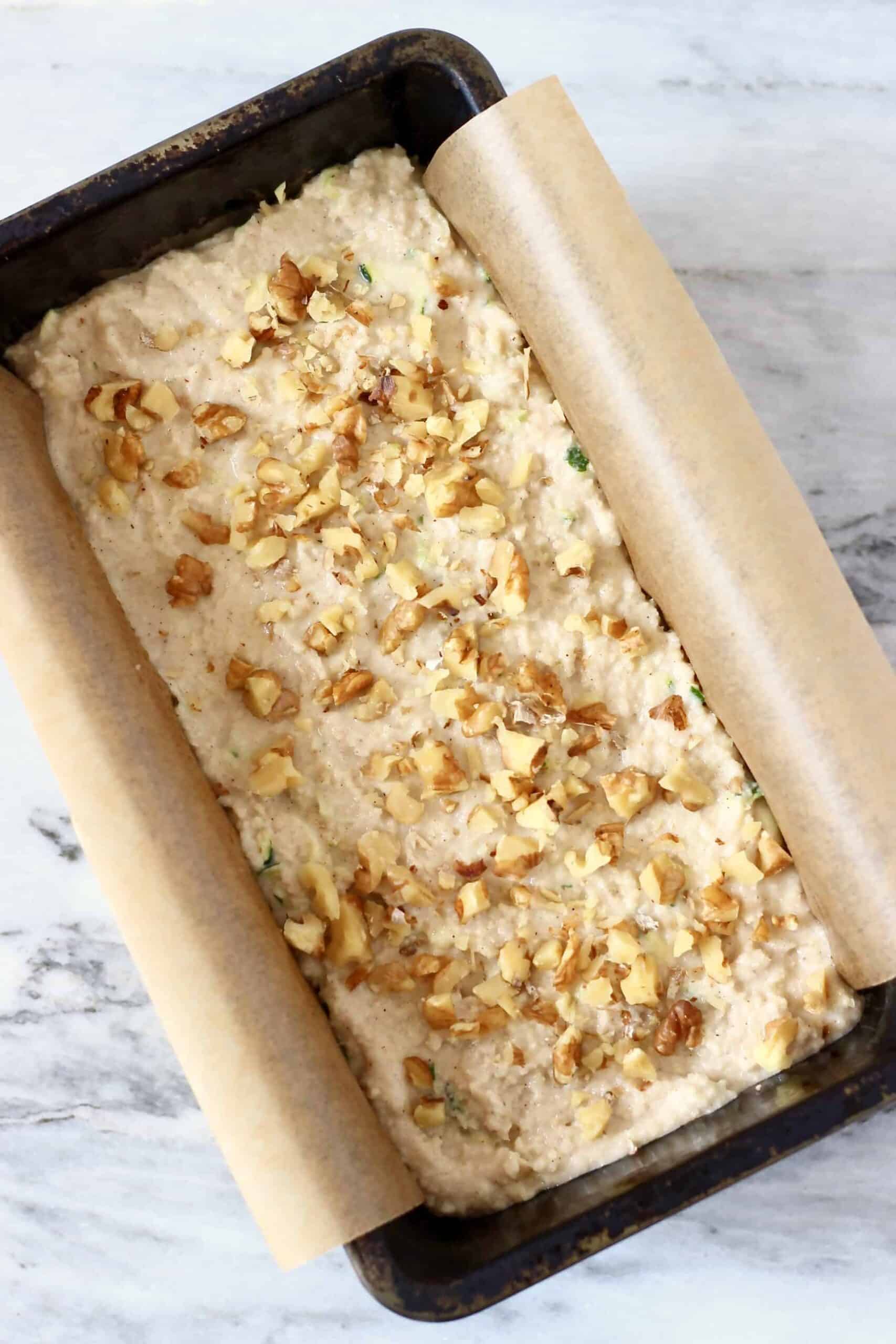 This Gluten-Free Vegan Zucchini Bread is seriously moist, perfectly dense and subtly fragrant. It's made with grated zucchini and subtly spiced with cinnamon for a warm, toasty flavour. It makes the perfect dessert, breakfast, brunch or snack, especially for autumn/fall. #vegan #dairyfree #rhiansrecipes #zucchinibread #glutenfree #baking Raw gluten-free vegan zucchini bread batter in a loaf tin topped with chopped walnuts