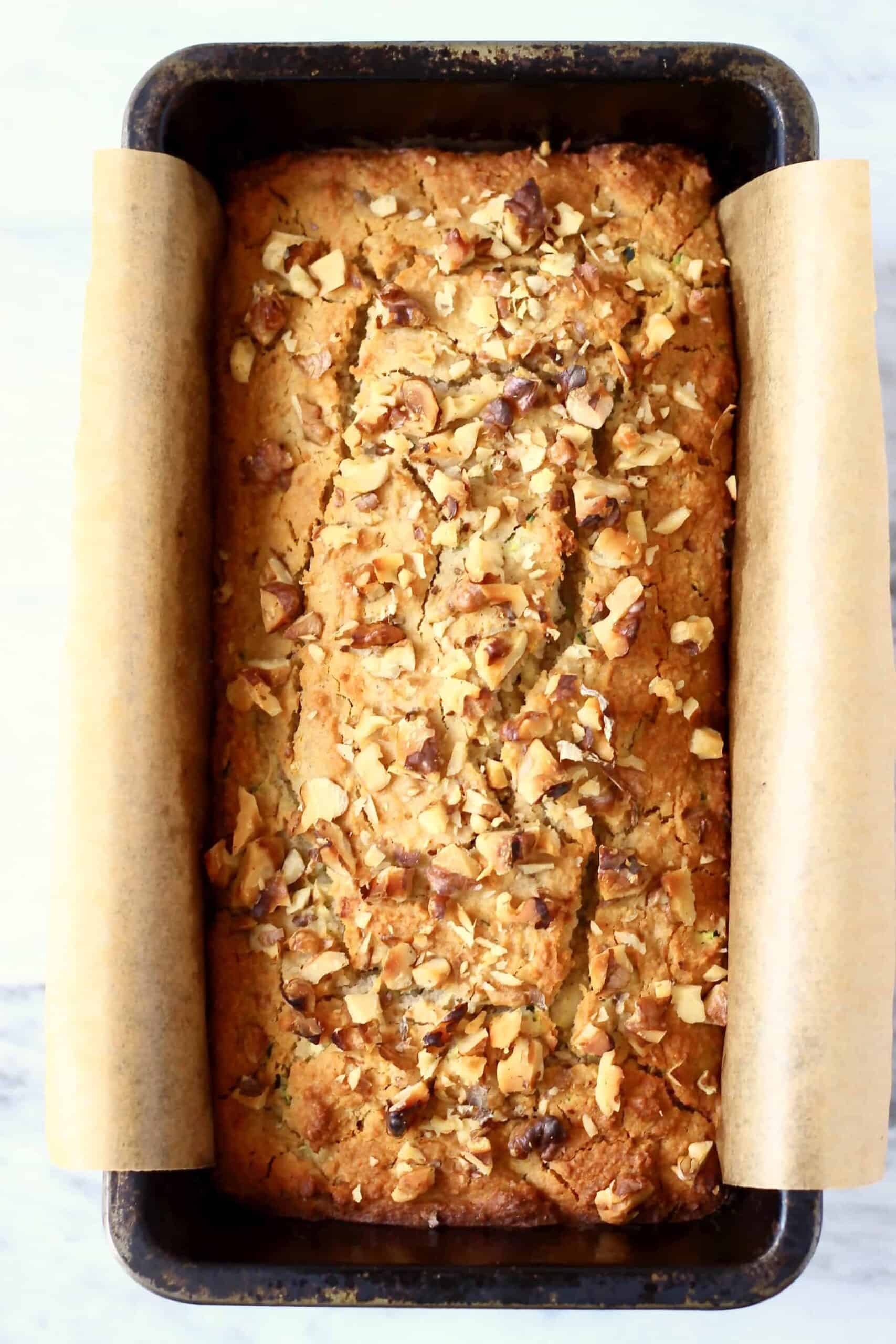 This Gluten-Free Vegan Zucchini Bread is seriously moist, perfectly dense and subtly fragrant. It's made with grated zucchini and subtly spiced with cinnamon for a warm, toasty flavour. It makes the perfect dessert, breakfast, brunch or snack, especially for autumn/fall. #vegan #dairyfree #rhiansrecipes #zucchinibread #glutenfree #baking A loaf of gluten-free vegan zucchini bread in a loaf tin lined with baking paper