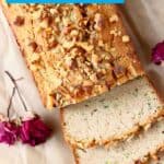 Photo of a loaf of zucchini bread with three slices against a sheet of brown baking paper with two red roses