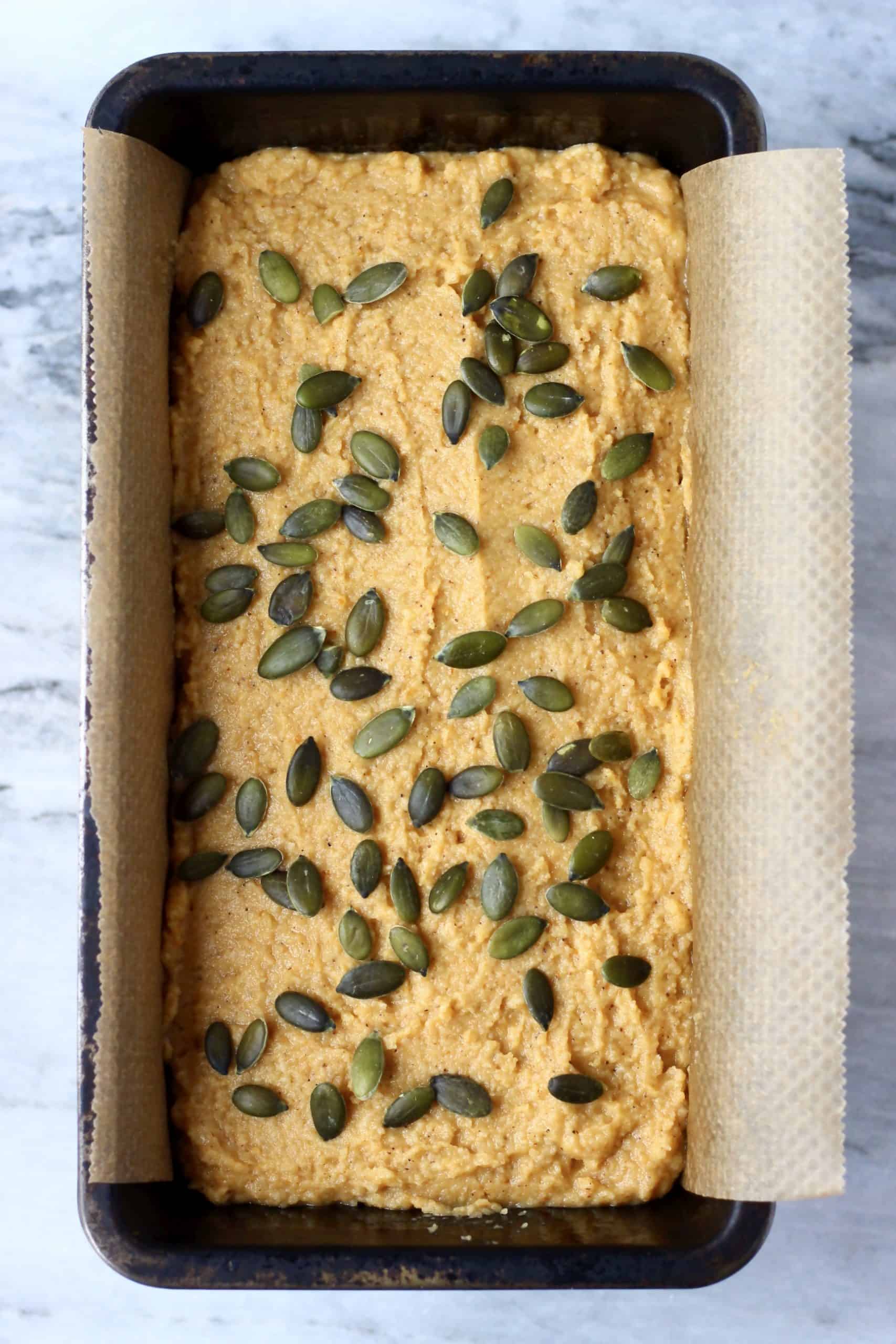 Gluten-free vegan pumpkin bread batter topped with pumpkin seeds in a loaf tin lined with baking paper