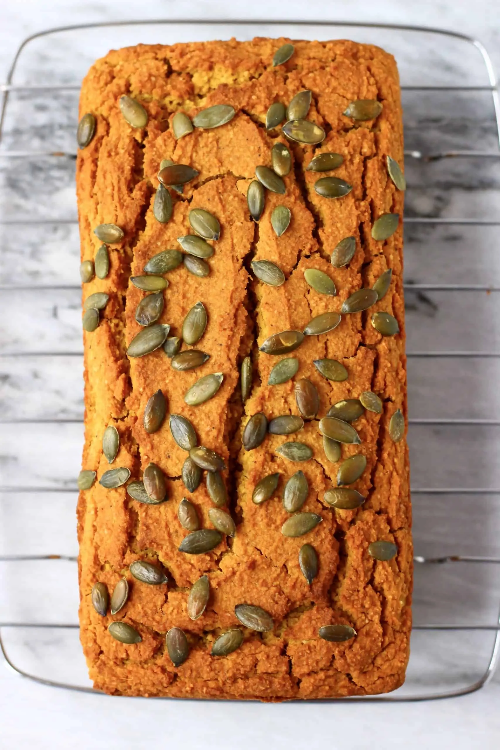 A loaf of gluten-free vegan pumpkin bread topped with pumpkin seeds on a wire rack