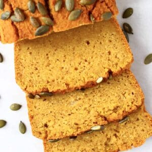 A loaf of gluten-free vegan pumpkin bread with three slices next to it
