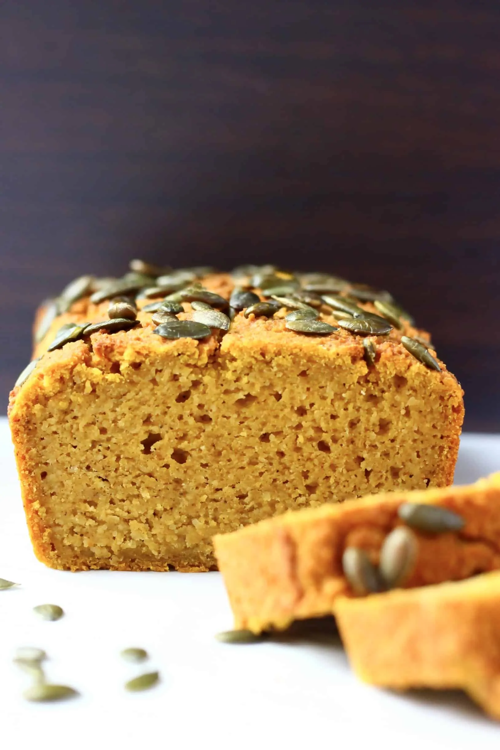 A sliced loaf of gluten-free vegan pumpkin bread topped with pumpkin seeds with two slices next to it