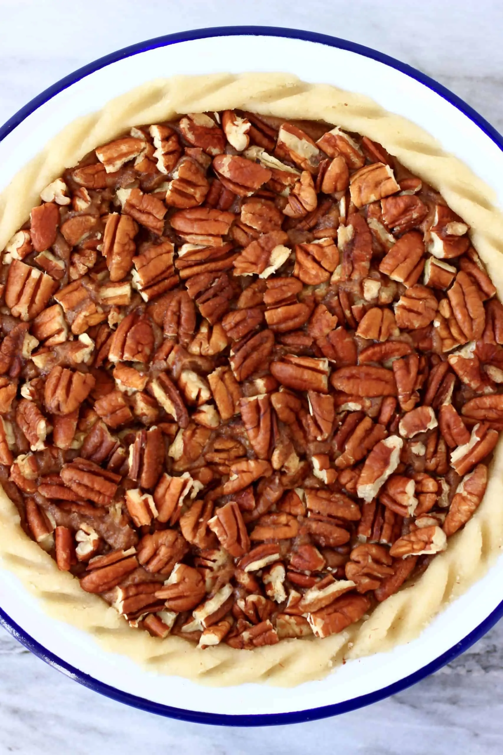 Raw gluten-free vegan pecan pie topped with chopped pecan nuts in a pie dish