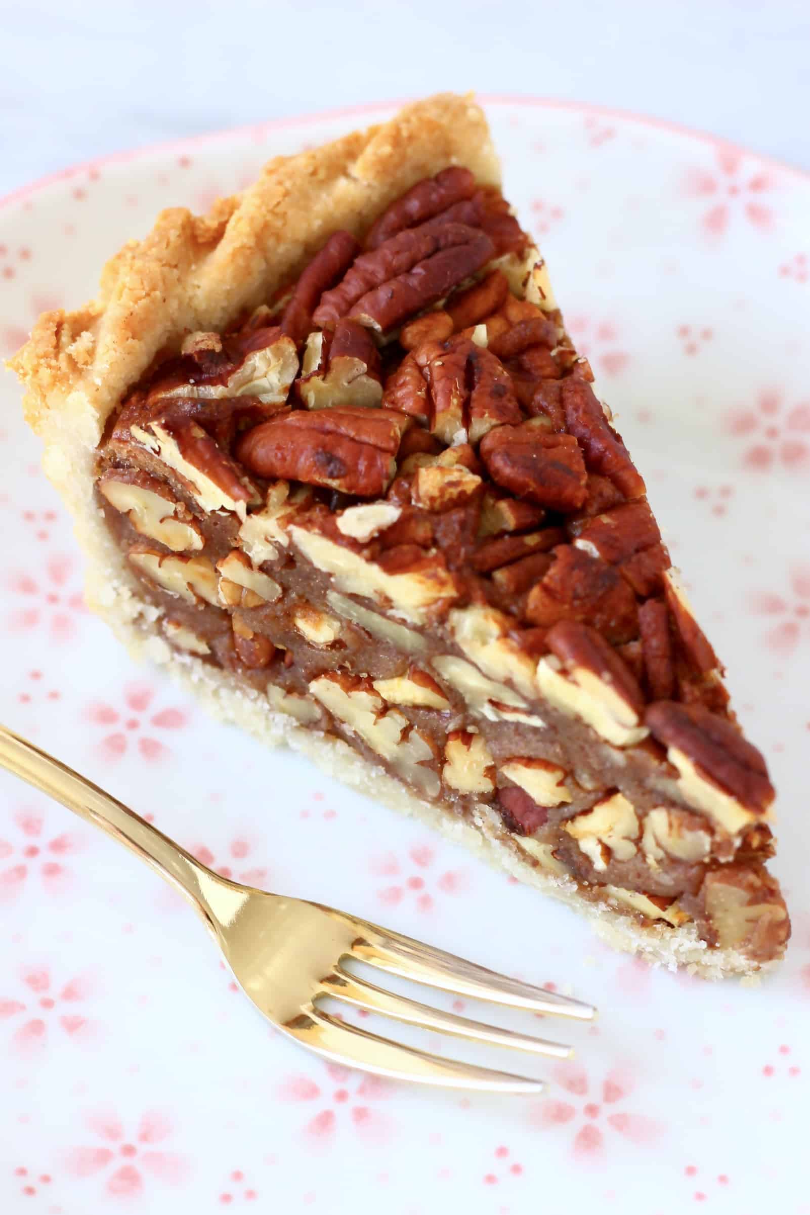 A slice of gluten-free vegan pecan pie on a plate with a gold fork