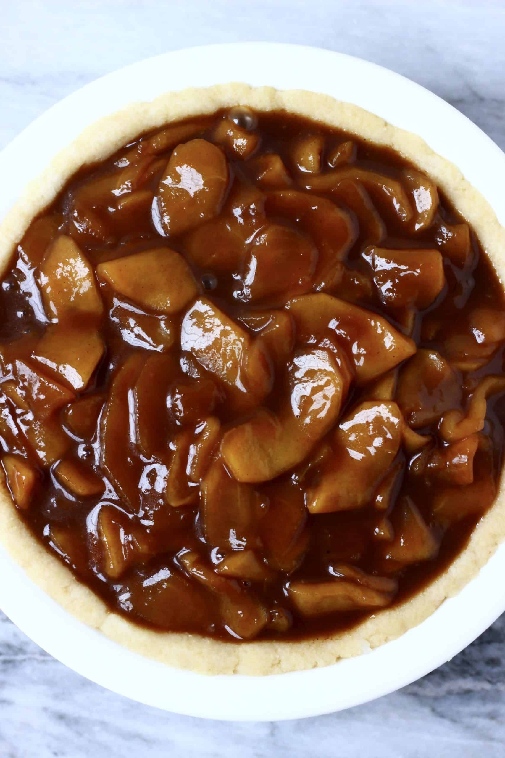 A raw pastry crust in a pie dish filled with cooked apple pie filling