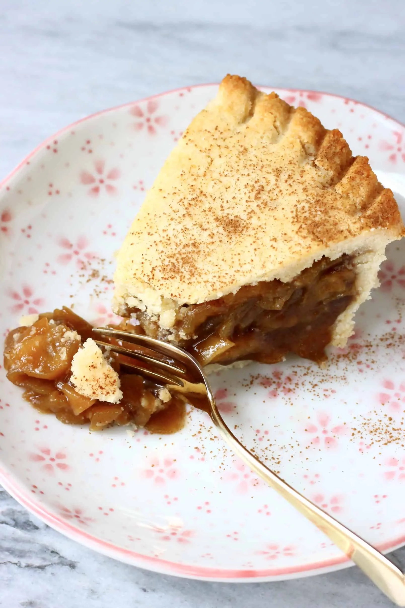 A slice of gluten-free vegan apple pie on a plate with a fork breaking off a piece