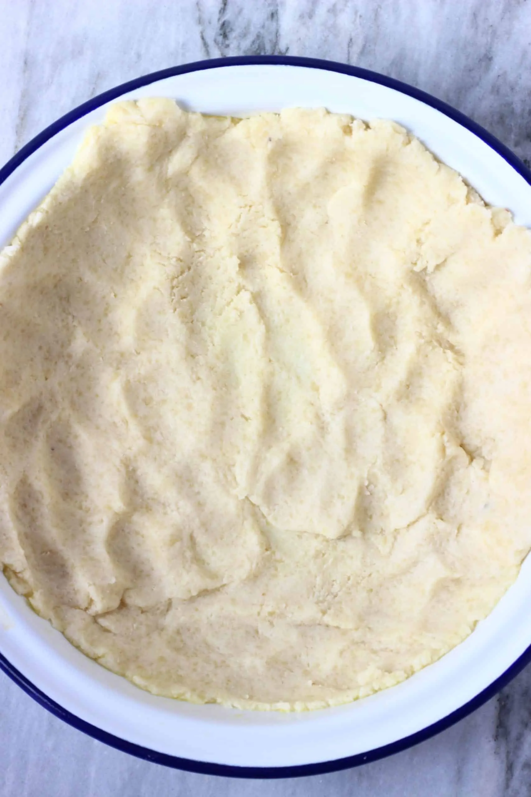 Gluten-free vegan pastry dough being pressed along the bottom of a pie dish