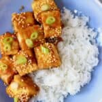 Photo of rice and several pieces of fried tofu sprinkled with sesame seeds and sliced spring onions on a blue plate
