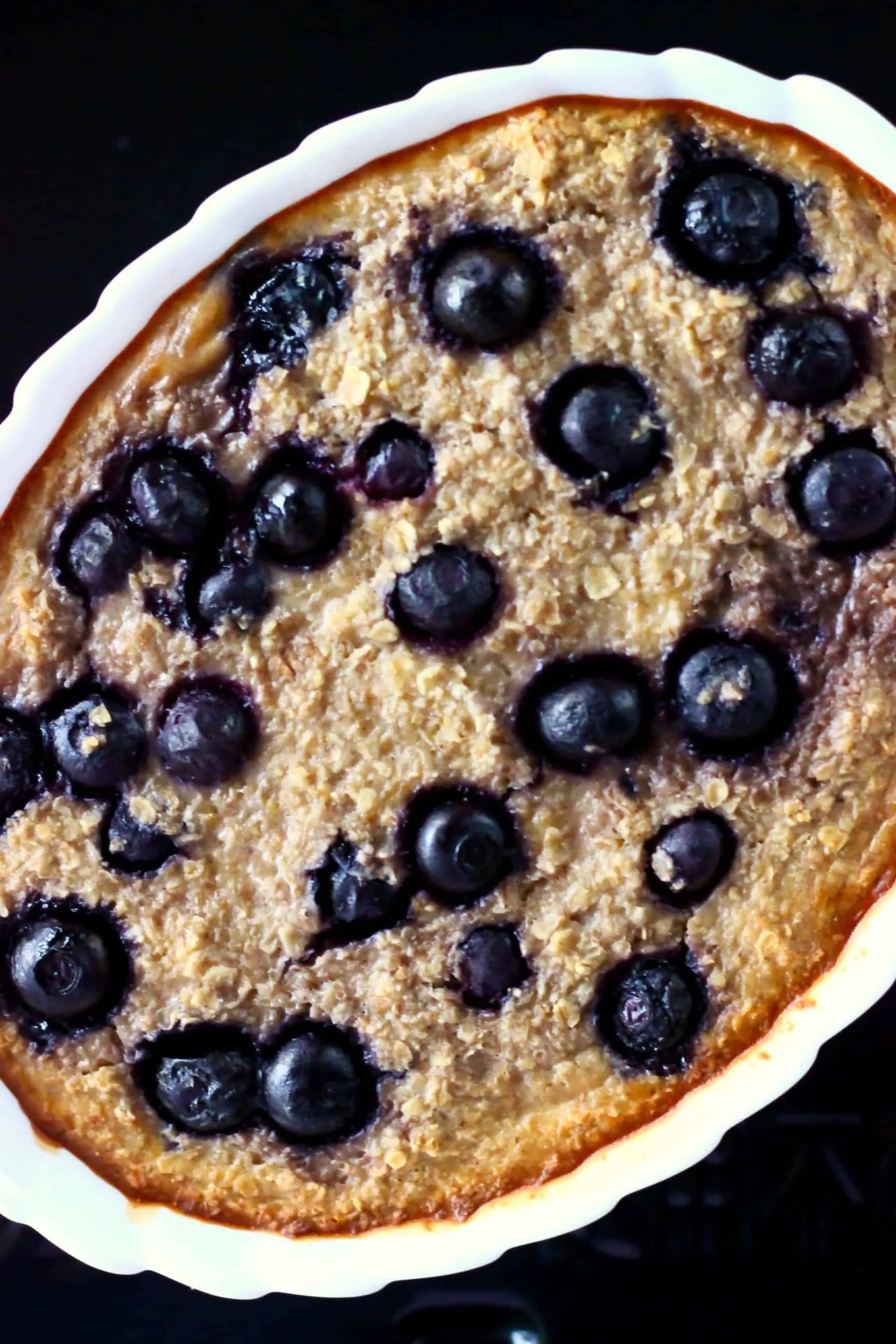 Blueberry banana baked oatmeal in a white oval baking dish against a black background