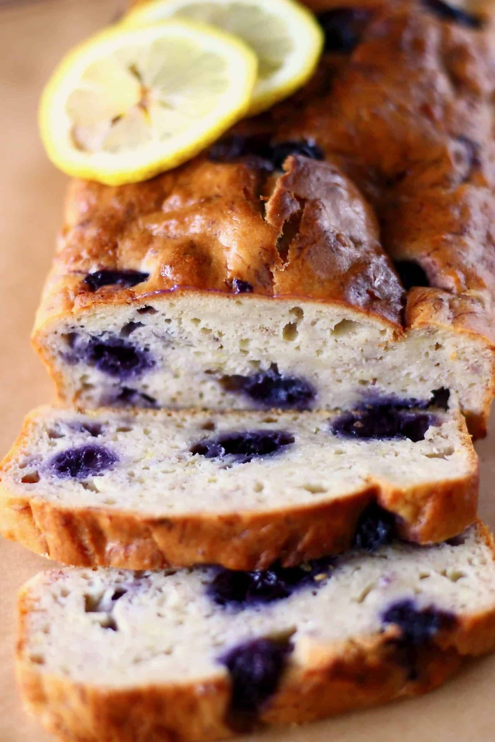 This Gluten-Free Vegan Lemon Blueberry Yogurt Cake is seriously moist, bright and citrusy, and packed full of jammy blueberries. It's perfect for dessert, breakfast, brunch or a snack. It's egg-free, dairy-free and refined sugar free. #vegan #glutenfree #dairyfree #blueberry #rhiansrecipes #vegancake Photo of a blueberry loaf cake with two slices of it next to it