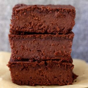 Three vegan black bean brownies stacked on top of each other against a grey background