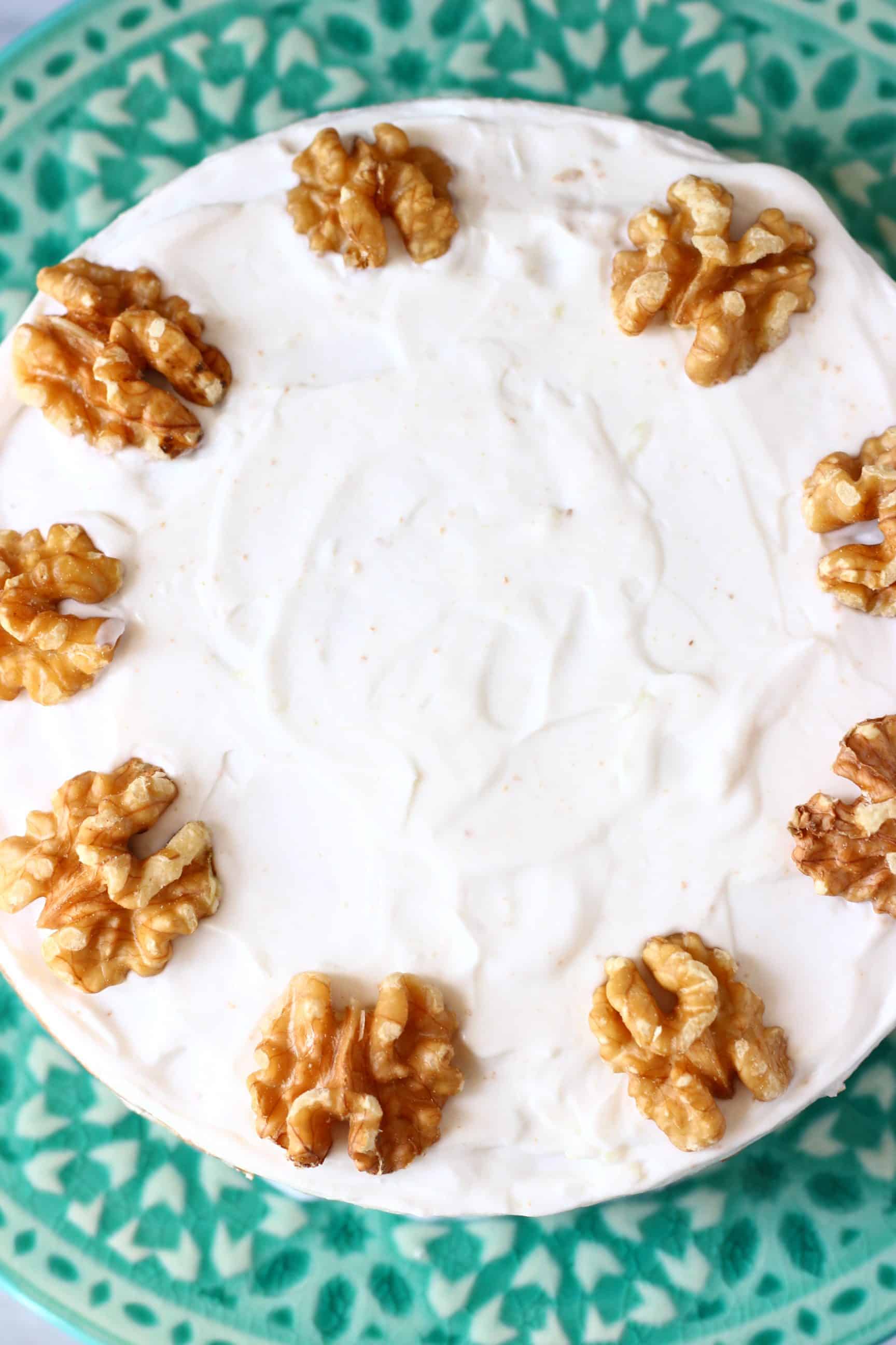 A vegan carrot cake topped with walnuts on a green cake stand