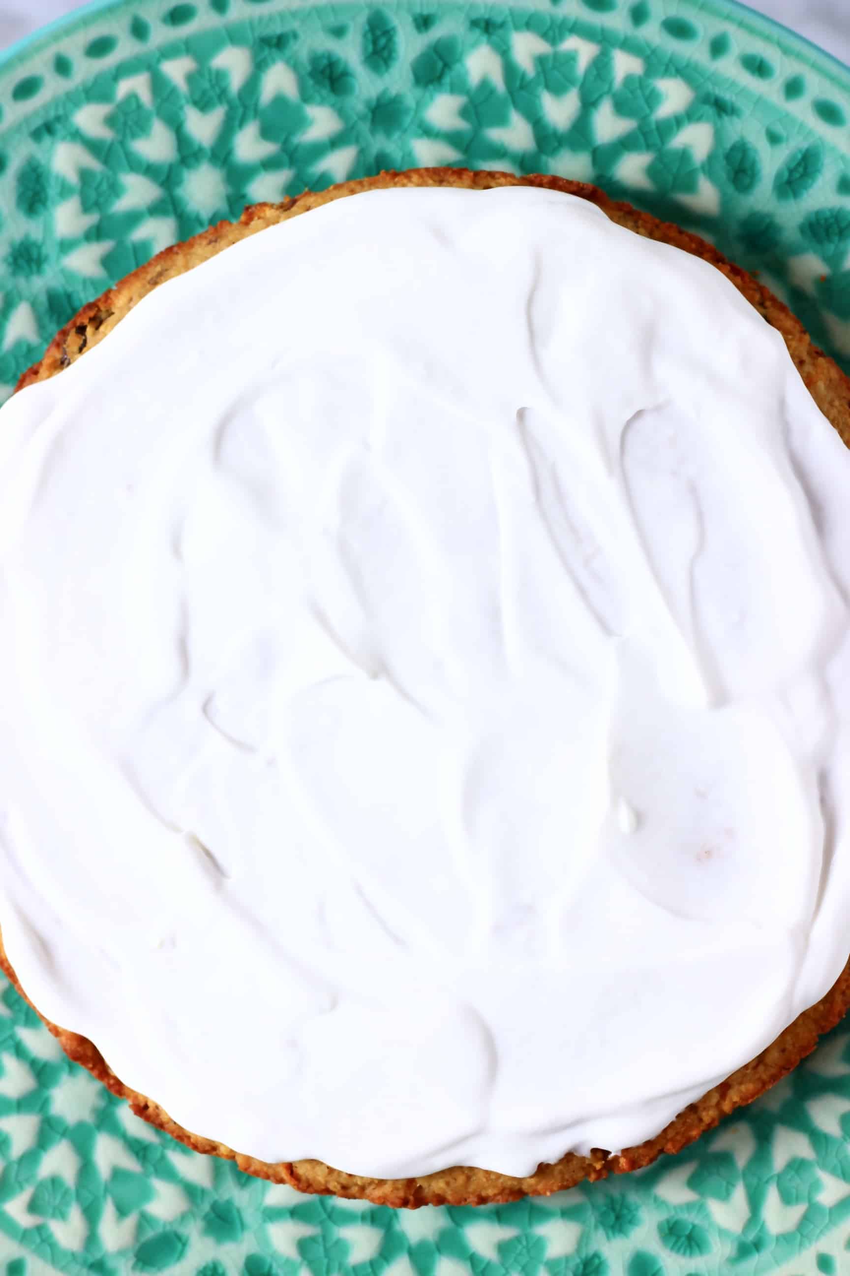 A green cake stand with vegan carrot cake on it topped with frosting