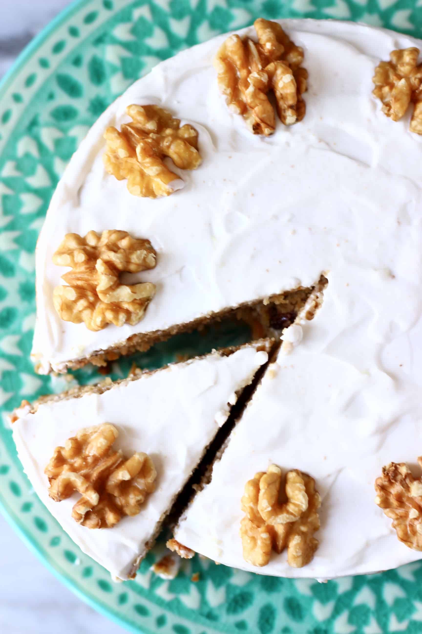 A vegan carrot cake topped with walnuts on a green cake stand with a slice cut out of it