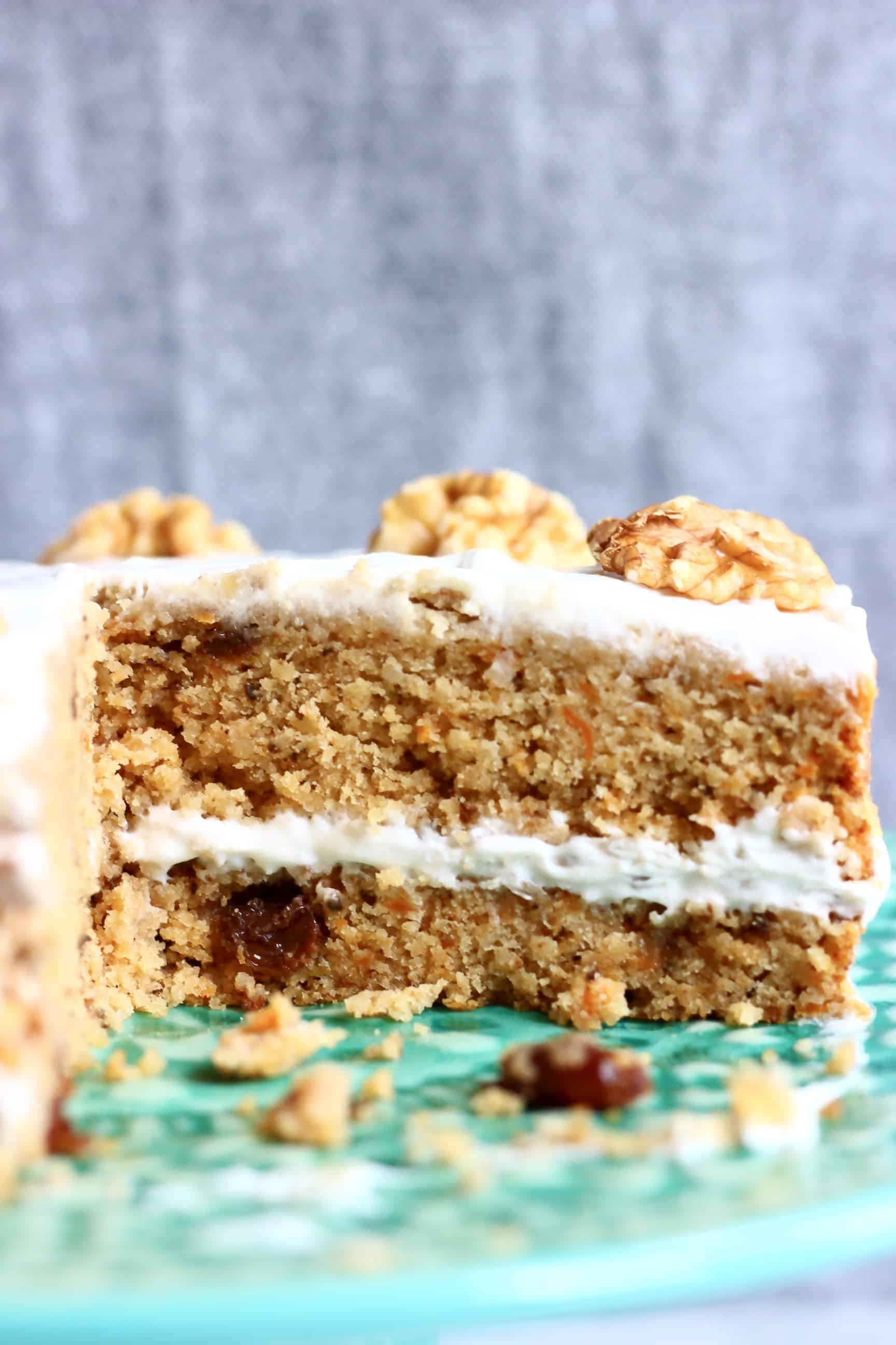 A sliced vegan carrot cake on a green cake stand with a grey background