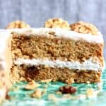 A sliced carrot cake on a green cake stand with a grey background