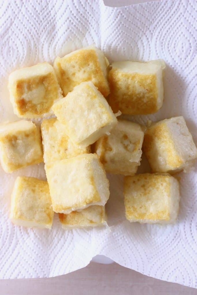 Golden brown cubes of tofu on a piece of white kitchen paper against a white background