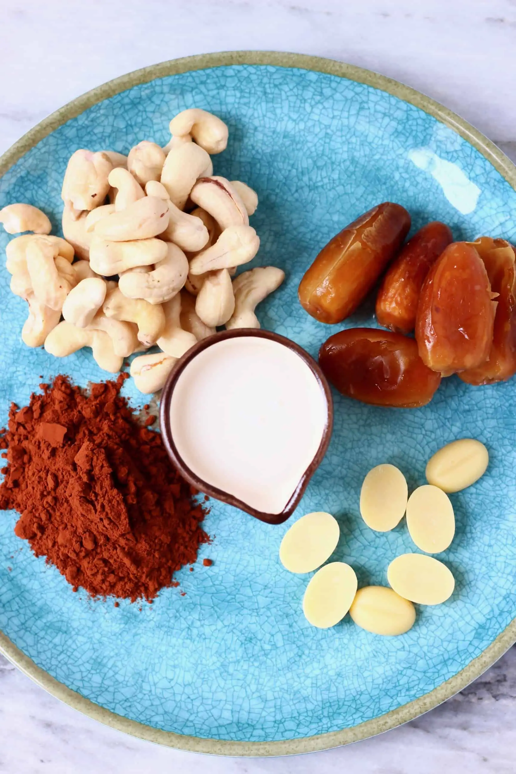 Cashew nuts, dates, cocoa powder, cacao butter and a small jug of milk on a plate