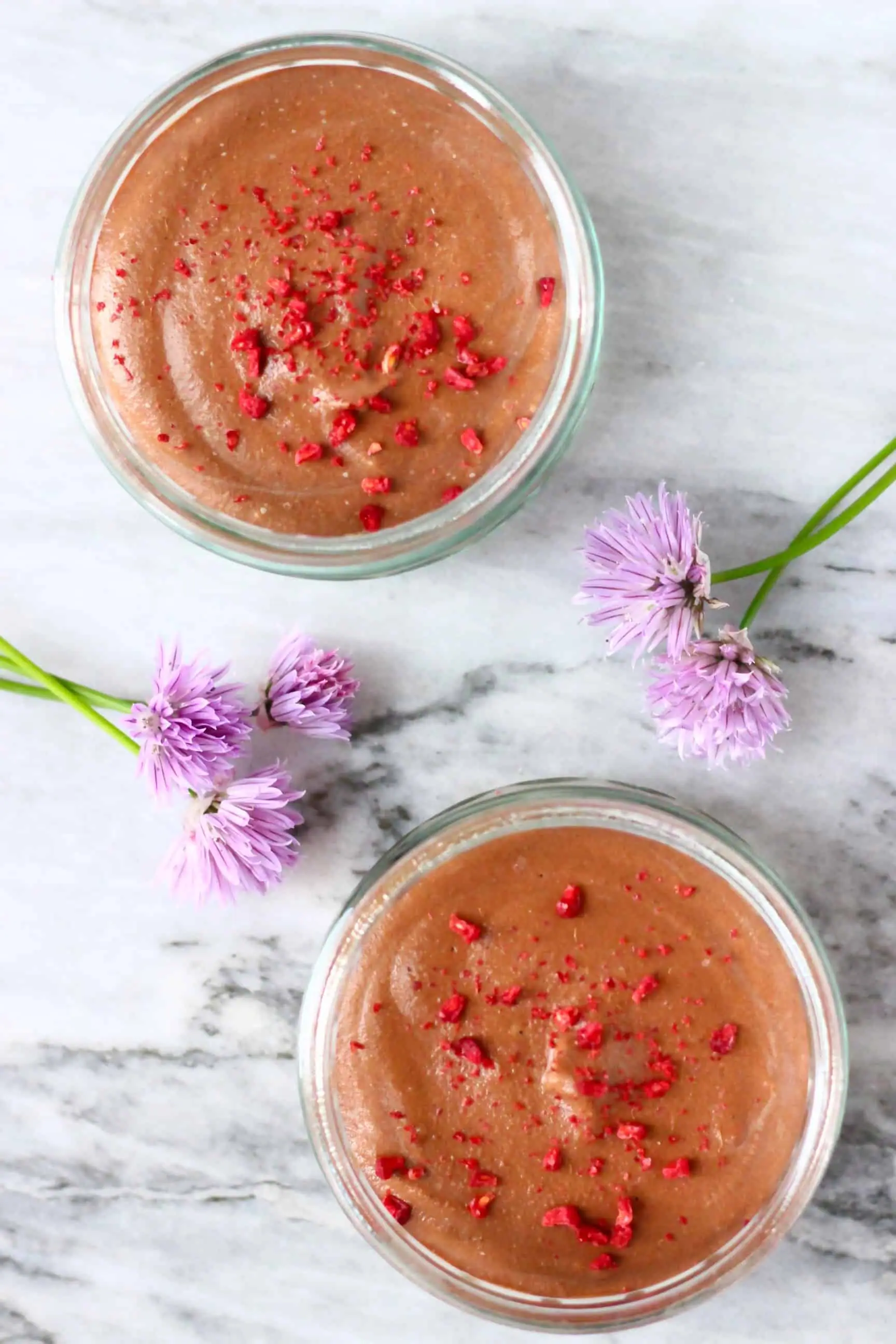 Two glass ramekins filled with vegan chocolate mousse topped with freeze-dried raspberries