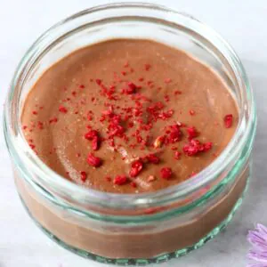Vegan chocolate mousse in a glass ramekin topped with freeze-dried raspberries