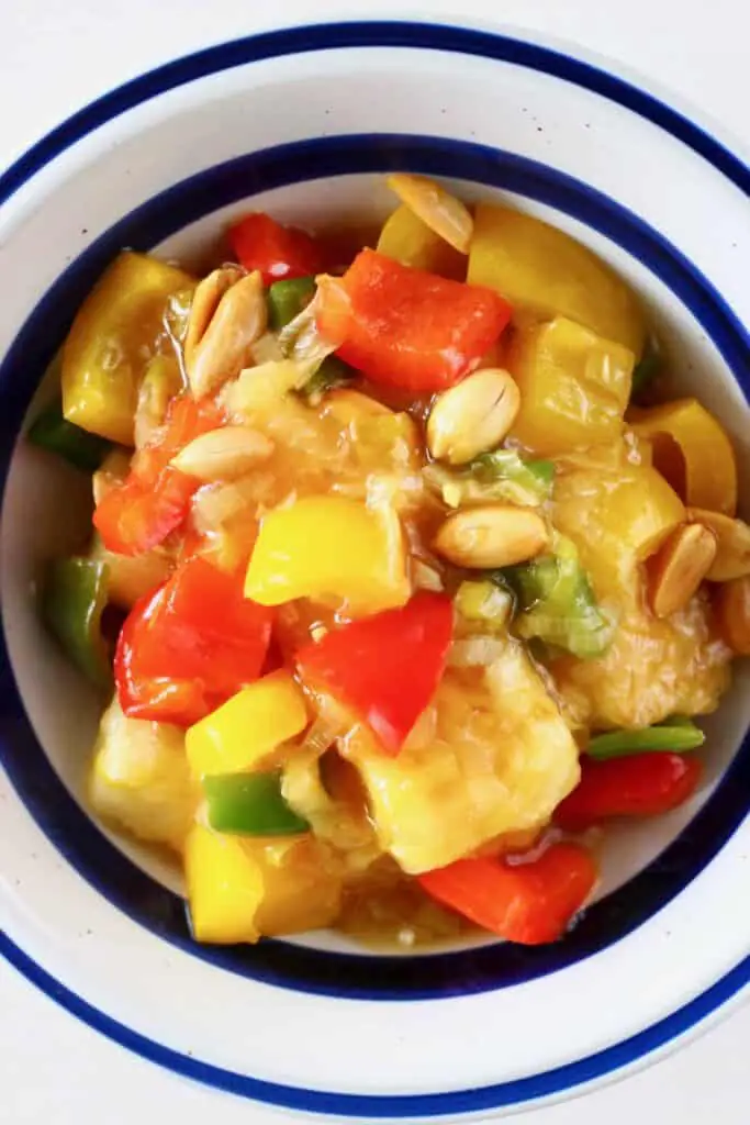 Photo of tofu cubes, peppers and peanuts in a white bowl with a blue rim