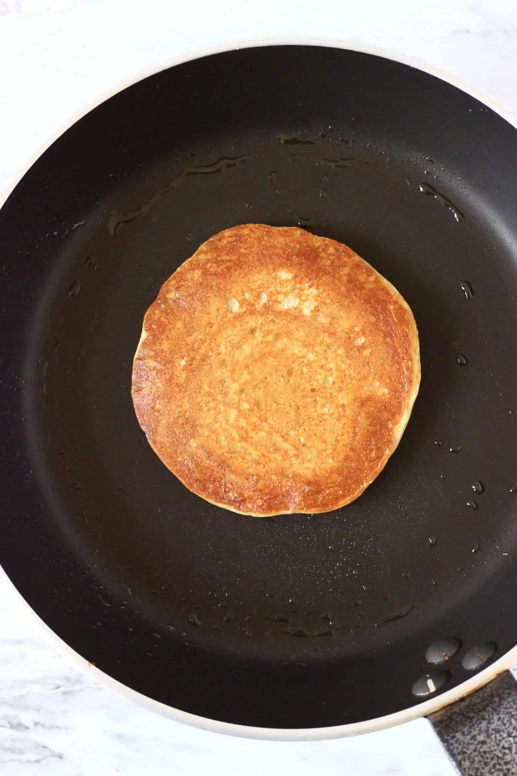 A golden brown gluten-free vegan protein pancake in a frying pan