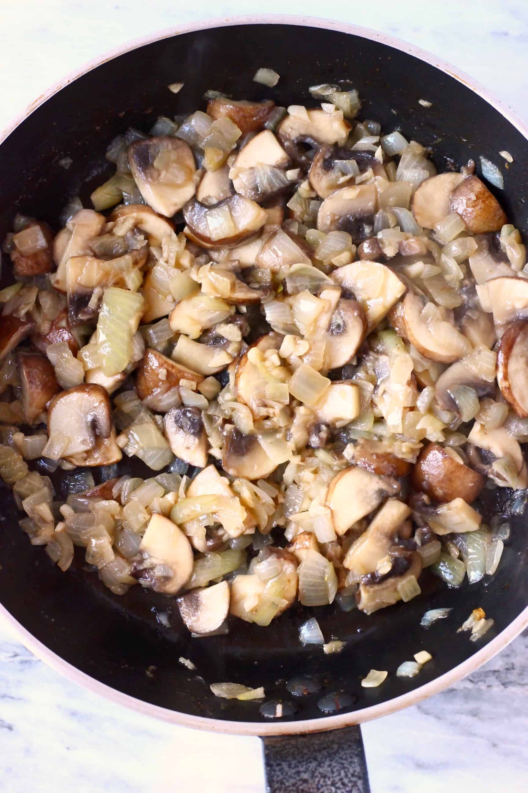 Diced onion and sliced mushrooms being fried in a black frying pan